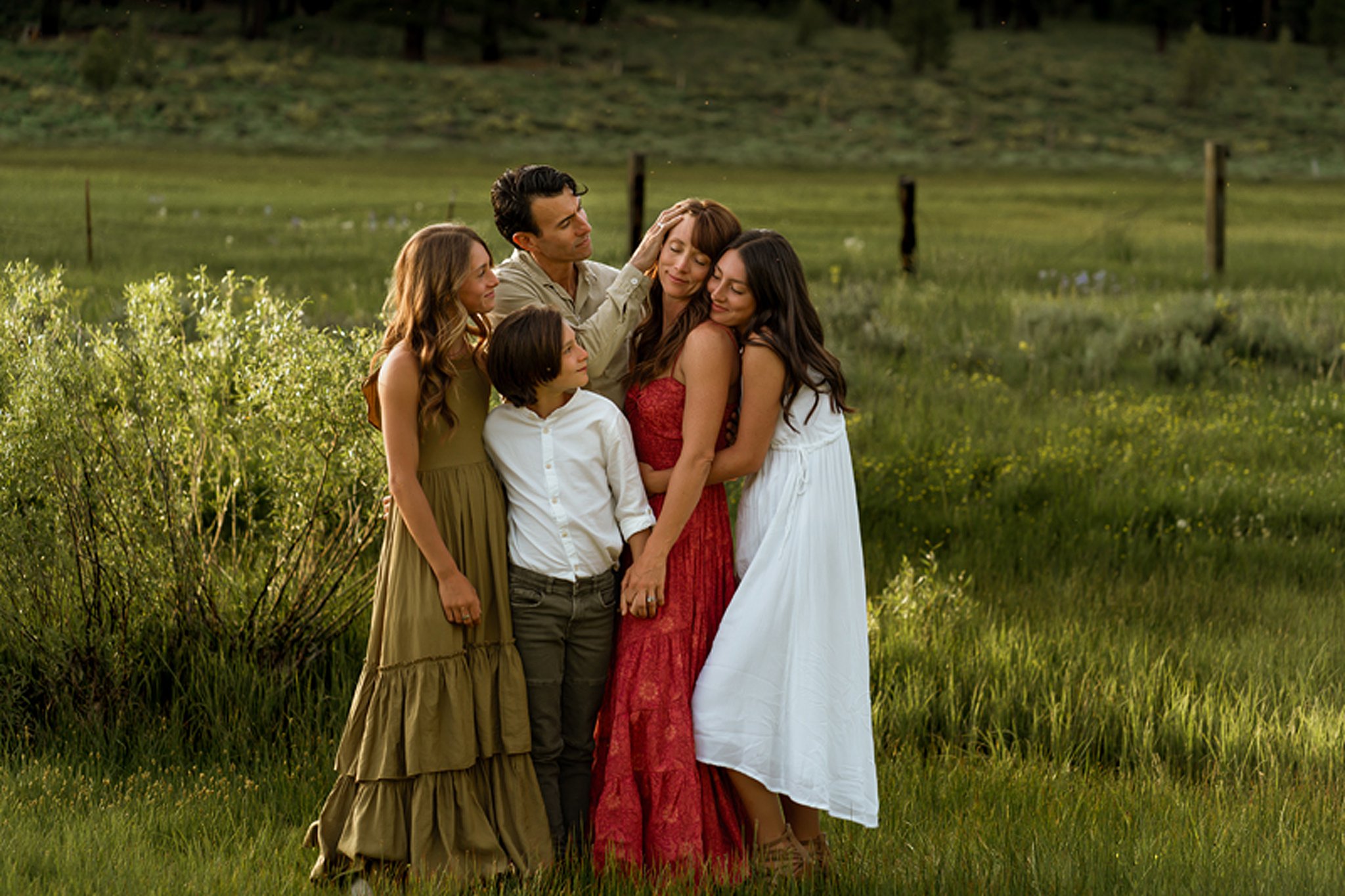 A mother in a red dress stands in a field of tall green grass is hugged and held by her family in the parks in sparks