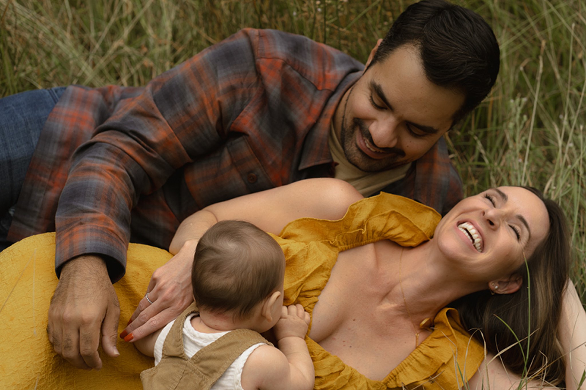 Happy parents lay in a field of grass while playing with their infant baby at one of the truckee parks